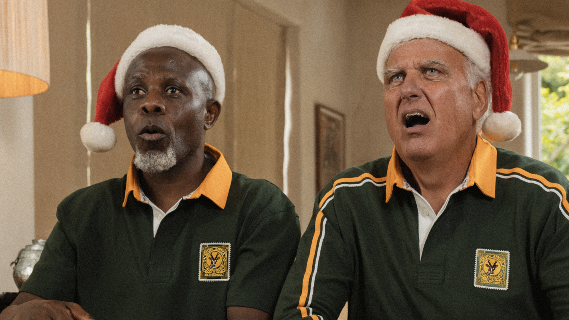 Two men in Springbok polos and Santa hats mid-carol, Old School Christmas gifting